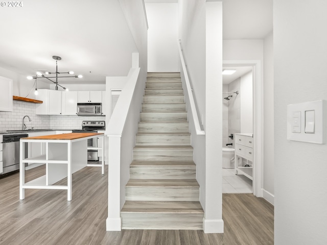 stairway with a chandelier, sink, and wood-type flooring