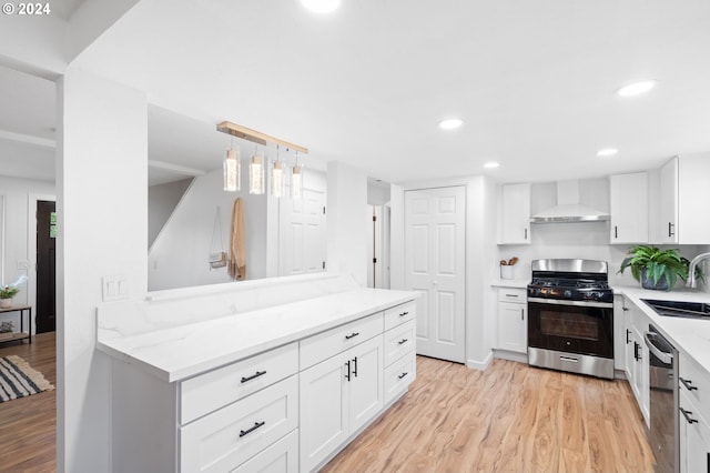 kitchen with white cabinetry, sink, wall chimney range hood, light hardwood / wood-style flooring, and appliances with stainless steel finishes