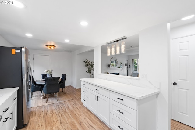 kitchen with stainless steel refrigerator, light stone countertops, white cabinetry, hanging light fixtures, and light wood-type flooring