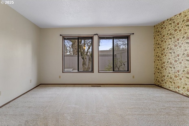 empty room featuring light carpet, a textured ceiling, baseboards, and wallpapered walls