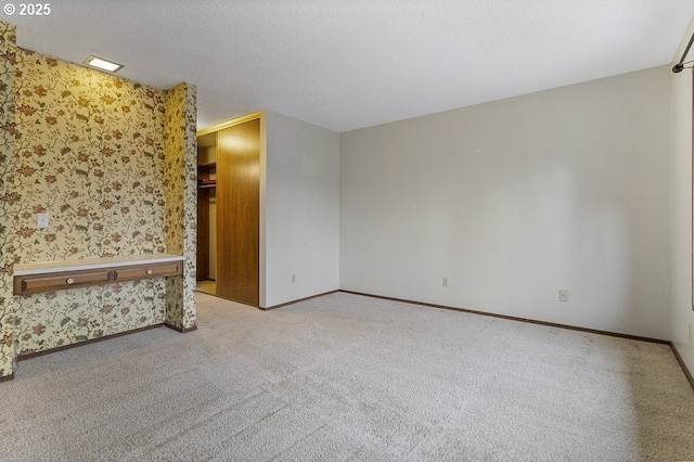 unfurnished room featuring a textured ceiling, wallpapered walls, light carpet, and baseboards