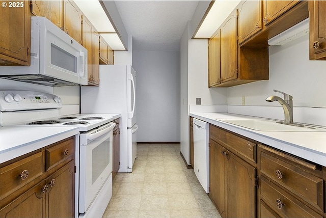 kitchen with brown cabinetry, white appliances, light countertops, and a sink