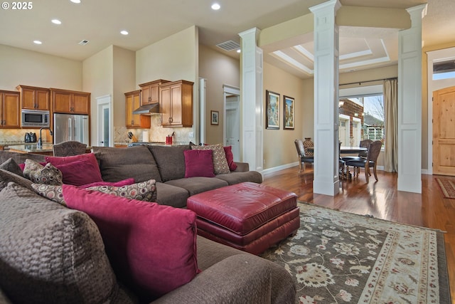 living room featuring dark wood-style flooring, recessed lighting, ornate columns, visible vents, and baseboards