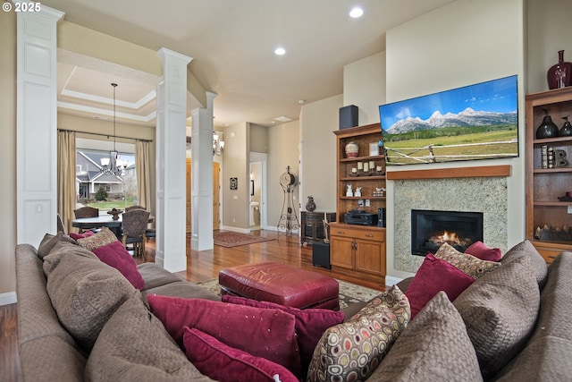 living area with a glass covered fireplace, a notable chandelier, ornate columns, and wood finished floors