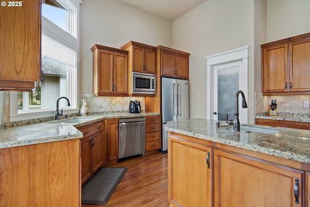 kitchen featuring light stone countertops, appliances with stainless steel finishes, brown cabinetry, and a sink