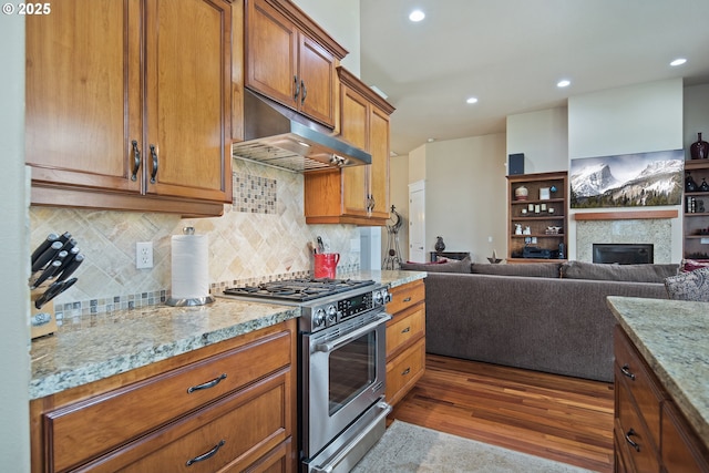 kitchen featuring brown cabinets, high end stainless steel range, dark wood-type flooring, light stone countertops, and under cabinet range hood