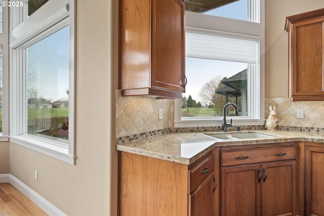 kitchen featuring tasteful backsplash, baseboards, brown cabinetry, light wood-style flooring, and a sink