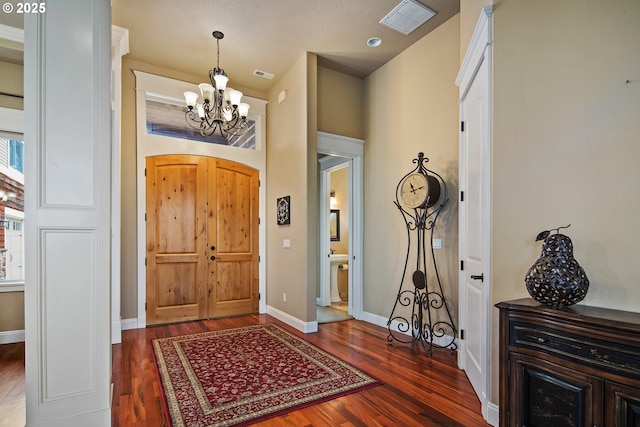 entrance foyer featuring dark wood-style flooring, visible vents, a notable chandelier, and baseboards