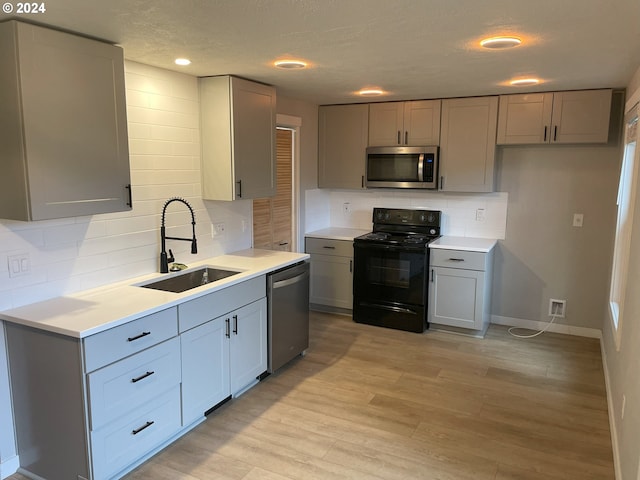 kitchen featuring appliances with stainless steel finishes, sink, a textured ceiling, light hardwood / wood-style floors, and decorative backsplash