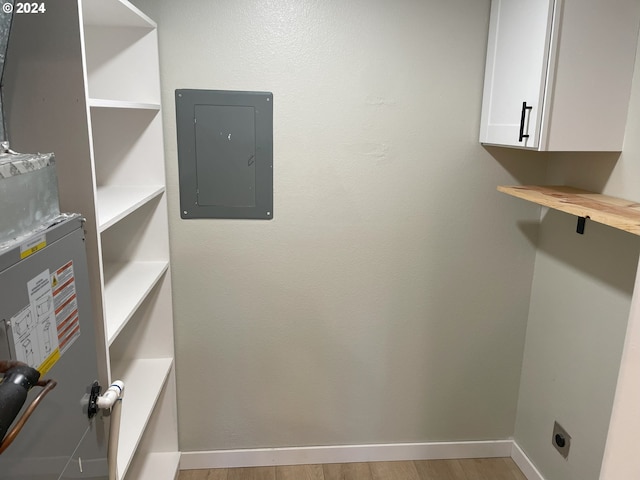 washroom with electric dryer hookup, cabinets, electric panel, and light wood-type flooring