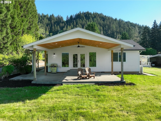 back of house with a lawn, a forest view, ceiling fan, french doors, and a patio area