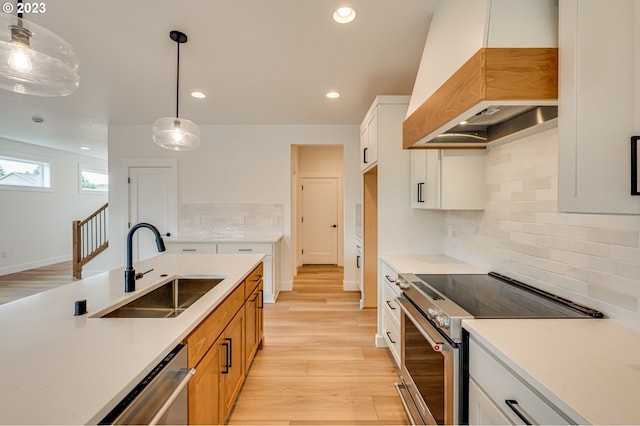 kitchen with white cabinets, custom exhaust hood, pendant lighting, sink, and appliances with stainless steel finishes