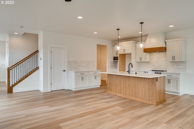 kitchen with premium range hood, a center island with sink, and light wood-type flooring