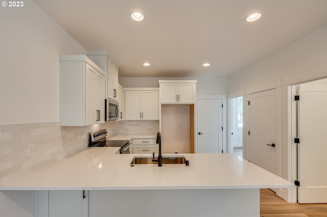 kitchen with white cabinets, sink, kitchen peninsula, appliances with stainless steel finishes, and light hardwood / wood-style floors