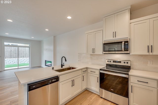 kitchen featuring light wood-type flooring, sink, white cabinetry, kitchen peninsula, and stainless steel appliances