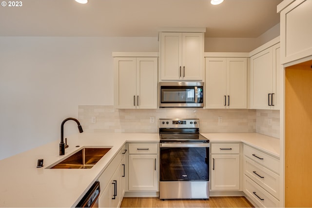 kitchen with appliances with stainless steel finishes, light hardwood / wood-style floors, white cabinetry, and sink