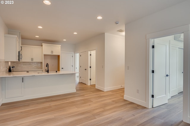 kitchen with light wood-type flooring, backsplash, white cabinetry, and sink