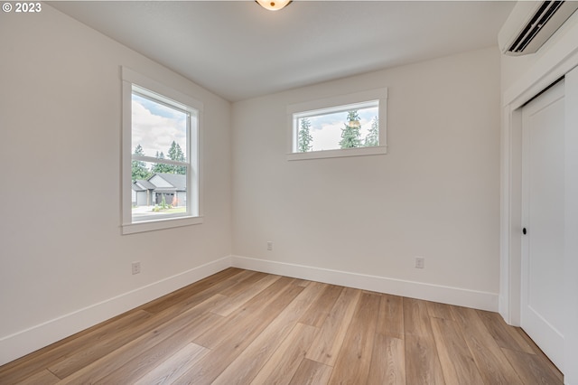 unfurnished bedroom featuring light hardwood / wood-style floors, multiple windows, and an AC wall unit