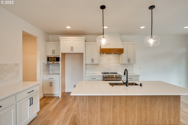 kitchen featuring an island with sink, decorative light fixtures, and premium range hood