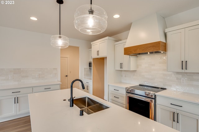 kitchen featuring sink, stainless steel range with electric cooktop, white cabinetry, custom range hood, and decorative light fixtures