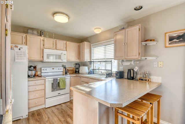 kitchen with a kitchen bar, light hardwood / wood-style floors, kitchen peninsula, sink, and white appliances