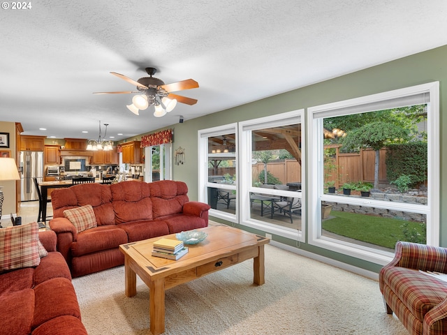 living room with a textured ceiling, ceiling fan with notable chandelier, and light carpet