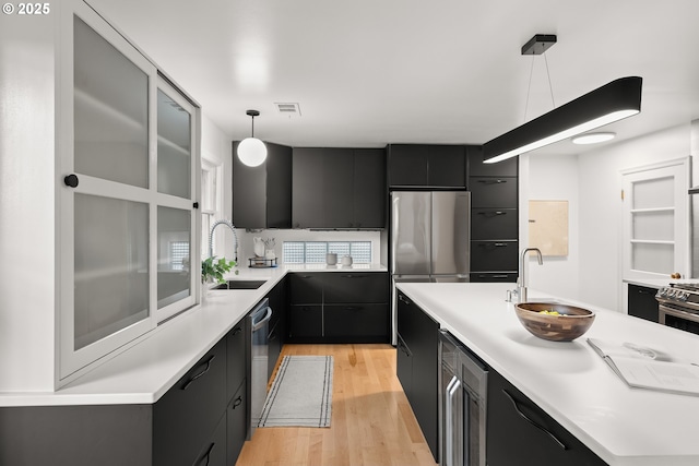 kitchen featuring sink, appliances with stainless steel finishes, hanging light fixtures, and light hardwood / wood-style flooring