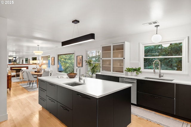 kitchen with an island with sink, stainless steel dishwasher, hanging light fixtures, and sink