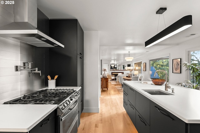 kitchen with a center island with sink, hanging light fixtures, wall chimney exhaust hood, gas range, and tasteful backsplash