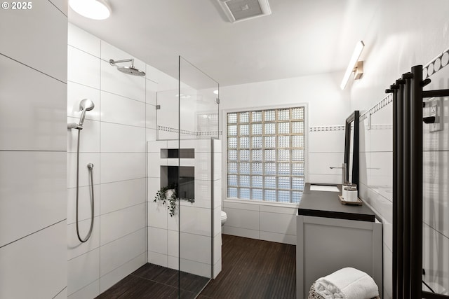 bathroom featuring toilet, vanity, hardwood / wood-style flooring, and tiled shower