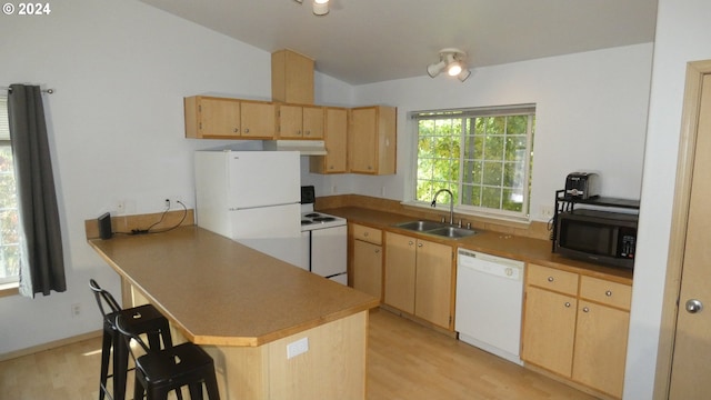 kitchen with light brown cabinets, a kitchen bar, light wood-type flooring, sink, and white appliances