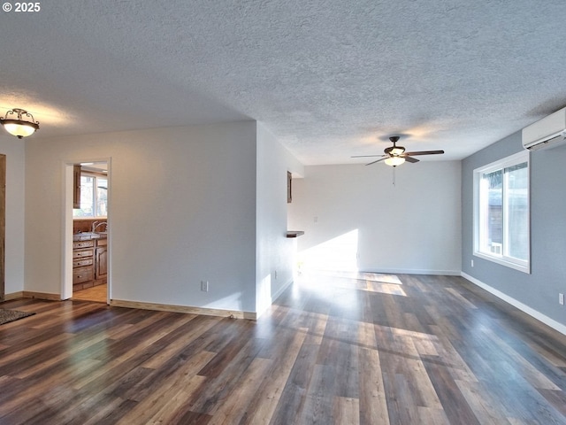 empty room featuring a textured ceiling, dark wood-type flooring, a wall mounted AC, and ceiling fan