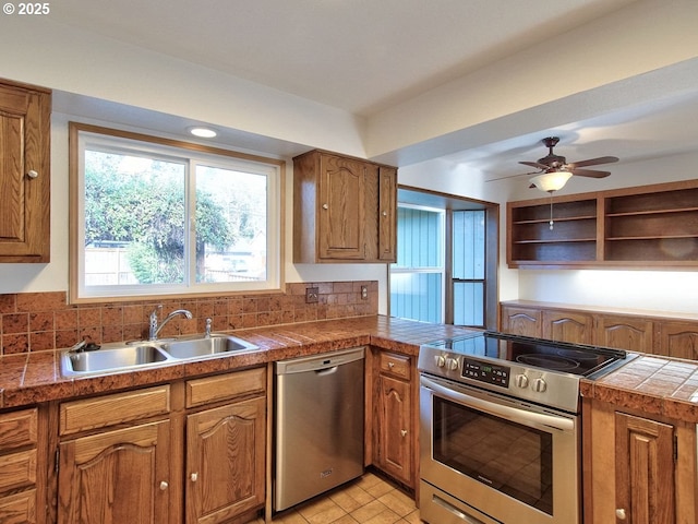 kitchen with appliances with stainless steel finishes, decorative backsplash, sink, ceiling fan, and tile countertops