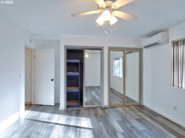 unfurnished bedroom with a wall mounted air conditioner, ceiling fan, hardwood / wood-style flooring, and two closets