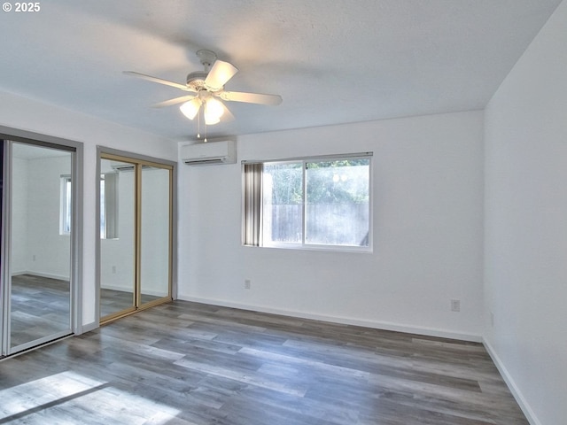 unfurnished bedroom with ceiling fan, a wall mounted AC, dark hardwood / wood-style floors, and two closets