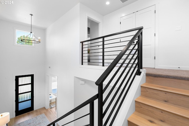 stairway with a high ceiling, wood-type flooring, and an inviting chandelier