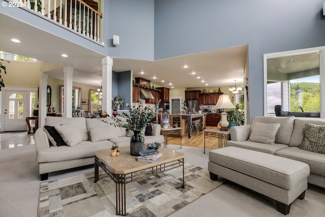 living room with an inviting chandelier, decorative columns, light colored carpet, and a high ceiling