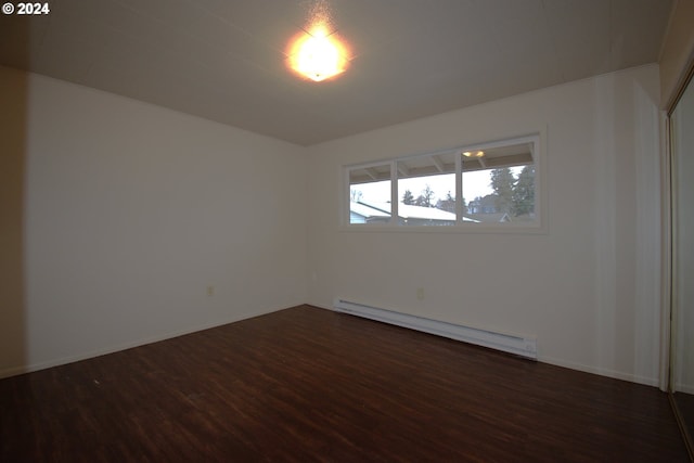 spare room with dark wood-type flooring and a baseboard heating unit