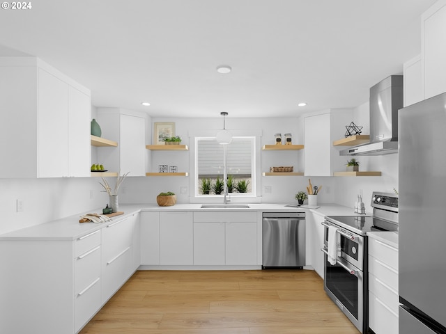 kitchen featuring wall chimney exhaust hood, white cabinetry, stainless steel appliances, and pendant lighting