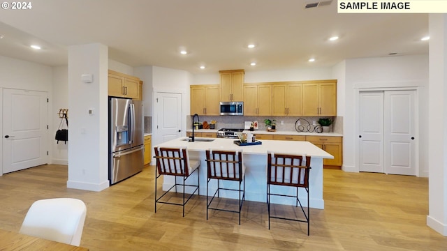 kitchen featuring a kitchen island with sink, sink, light wood-type flooring, and appliances with stainless steel finishes