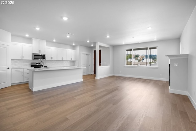 kitchen featuring white cabinets, stainless steel appliances, tasteful backsplash, light countertops, and an island with sink