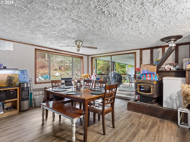 dining area with wood-type flooring, a wood stove, ceiling fan, crown molding, and a textured ceiling