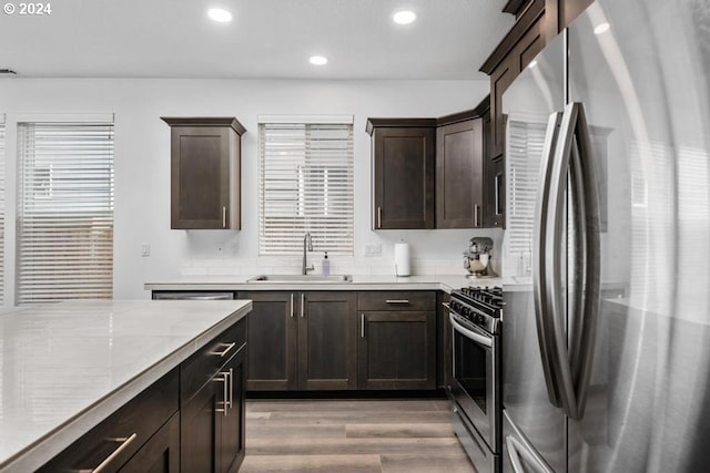 kitchen featuring sink, light wood-type flooring, appliances with stainless steel finishes, dark brown cabinets, and light stone counters