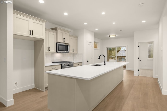 kitchen with tasteful backsplash, a center island with sink, appliances with stainless steel finishes, light wood-type flooring, and a sink