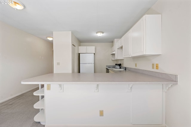 kitchen featuring kitchen peninsula, light colored carpet, white refrigerator, white cabinetry, and a breakfast bar area