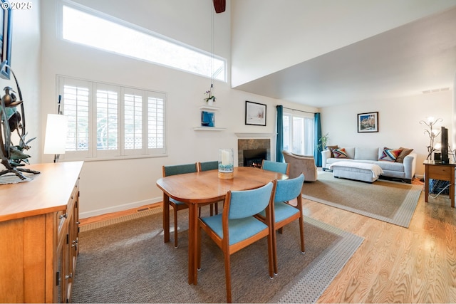 dining area featuring a high ceiling, a tiled fireplace, and wood finished floors