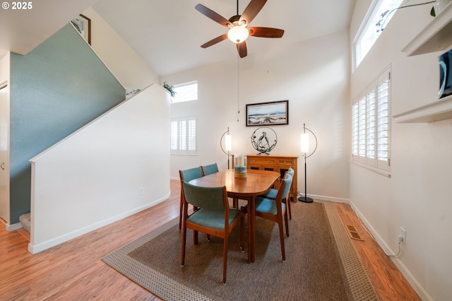 dining area featuring stairs, wood finished floors, a towering ceiling, ceiling fan, and baseboards