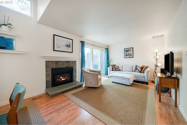 living room with a glass covered fireplace, baseboards, visible vents, and wood finished floors