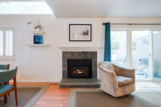 living area with a tiled fireplace, baseboards, visible vents, and wood finished floors