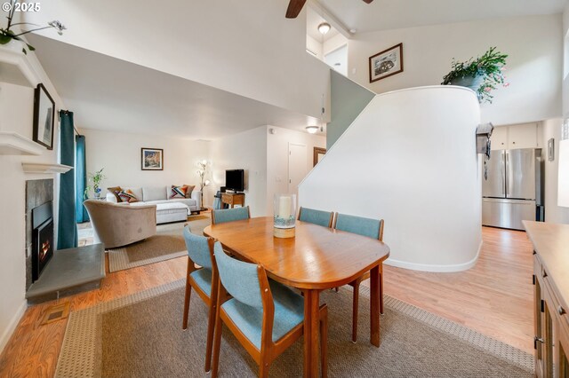 dining room featuring stairs, a towering ceiling, ceiling fan, light wood finished floors, and a tiled fireplace
